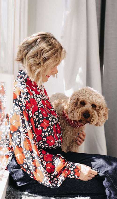 Britta sitzt am Fenster und schaut zu ihrem Hund, der Hund Cooper blickt in die Kamera